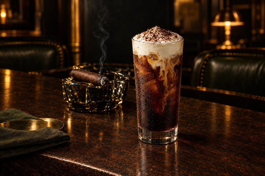 Tall iced cold brew topped with a floating layer of cream and grated dark chocolate, beside an unbanded maduro cigar